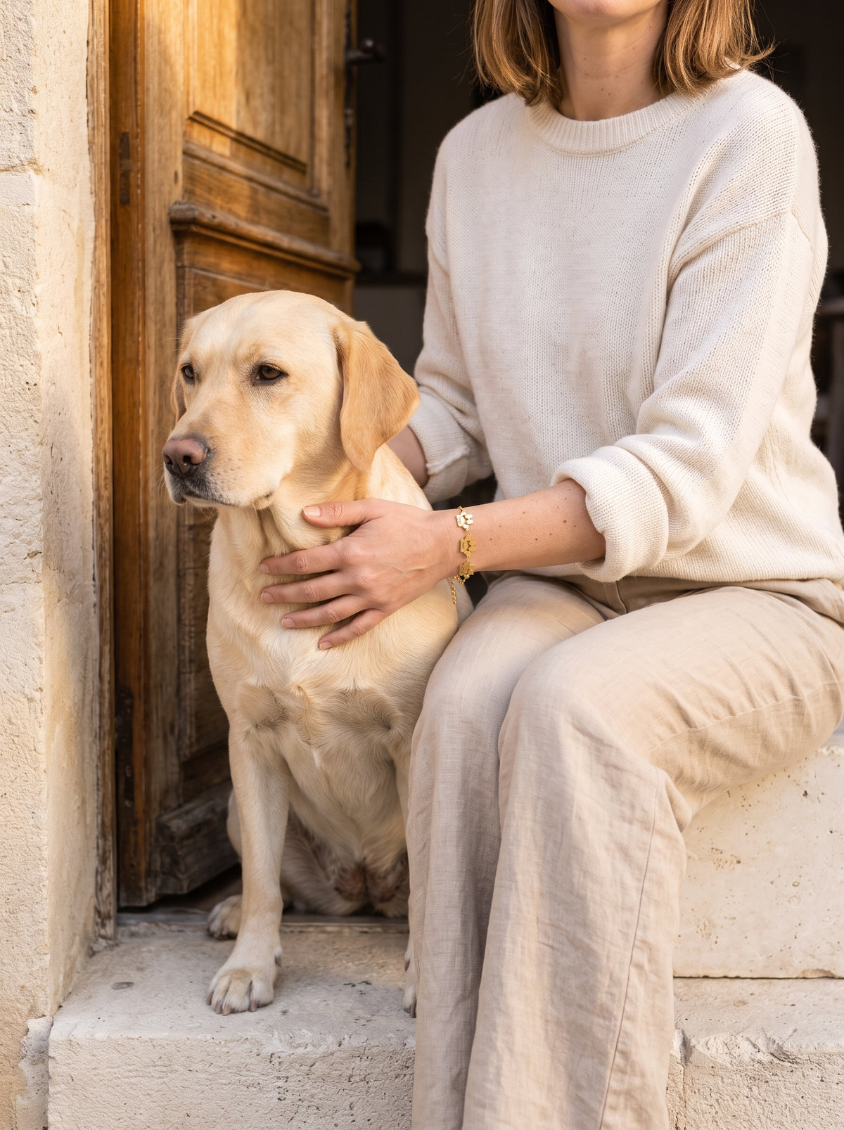 Femme assise sur le seuil d'une maison avec son labrador, bracelet patte en or au poignet